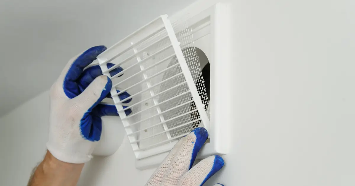 Person wearing white work gloves reinstalling or adjusting a white wall vent cover over an air duct opening.